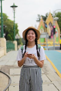 Portrait of smiling woman using mobile phone while standing against sky