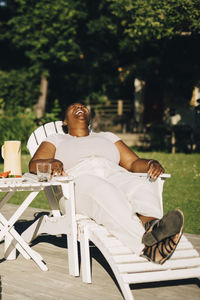Mid adult woman laughing while sitting on deck chair during garden party