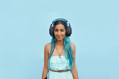 Portrait of young woman listening music against blue background