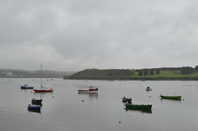 Boats in river against cloudy sky