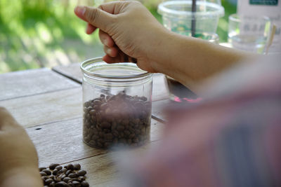 Midsection of person holding glass jar on table