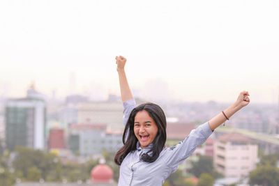 Portrait of smiling young woman standing against cityscape