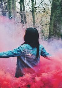 Rear view of woman amidst red smoke at forest