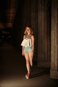 Full length of young woman standing on street in city at night
