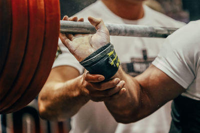 Midsection of man holding dumbbell in gym