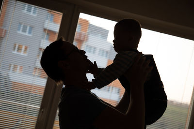 Silhouette father holding toddler son at home
