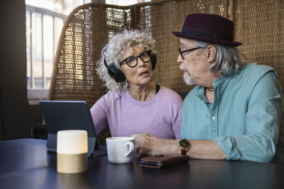 Senior couple sitting in cafe talking while working on digital tablet