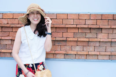 Portrait of young woman standing against brick wall