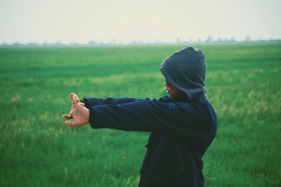 Side view of man stretching while standing on field against sky