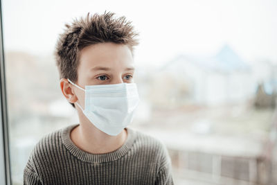 Close-up of boy wearing mask sitting by window at home