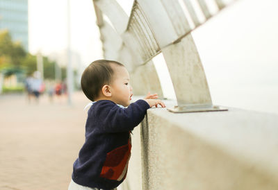 Side view of boy standing by railing in city
