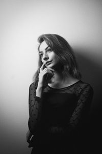 Beautiful young woman looking away while standing against wall