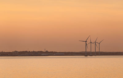 Wind turbines on shore against sky during sunset