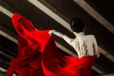 Rear view of tattooed seductive fashion model holding red fabric