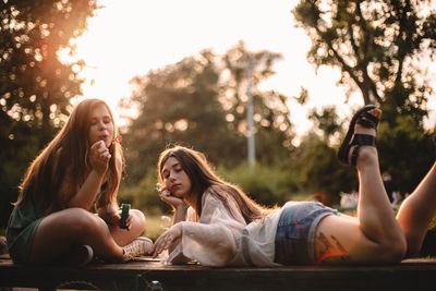 Young woman blowing bubbles while her girlfriend lying on bench