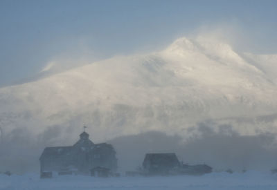 Houses against snowcapped mountains during foggy weather