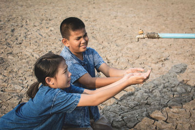Siblings with hands cupped below tap on cracked field