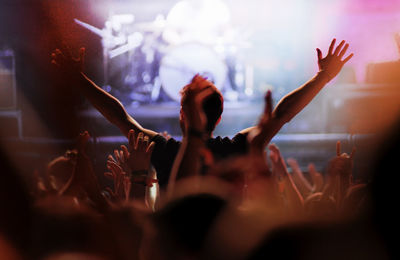 Rear view of man with arms outstretched at concert