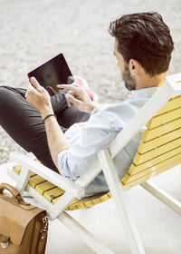 Rear view of businessman using digital tablet on lounge chair at park