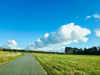 Empty road amidst field against sky