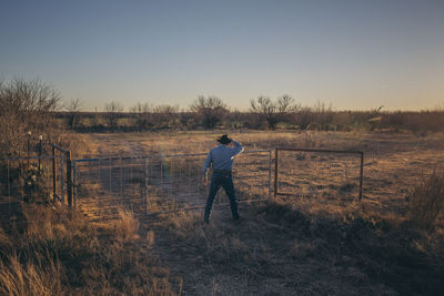 Rear view of man standing on field against clear sky