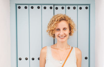 Portrait of smiling young woman standing by wall outdoors