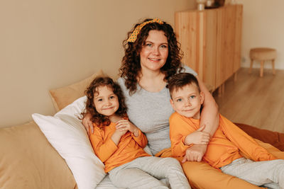 A happy mother hugs her children a little boy and a girl in pajamas sitting on bed in cozy interior 