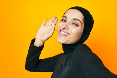 Portrait of smiling young woman against yellow background