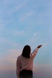 Rear view of woman with arms raised against sky during sunset