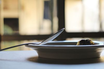 Close-up of food served in plate with spoon against window on table