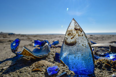 Close-up of broken glass at beach against blue sky
