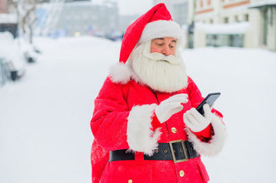 Portrait of smiling woman wearing santa claus costume standing on snow covered field