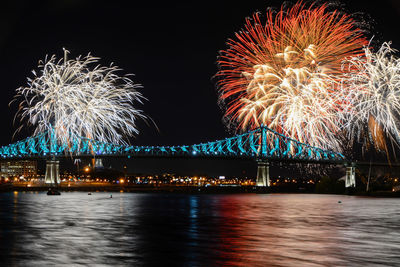 Low angle view of firework display over river against sky at night