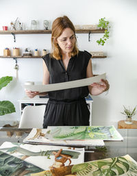 Creative female designer examining various paintings placed on table and working on project