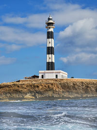 View from the sea of the black and white striped lighthouse on the coast of the island of menorca