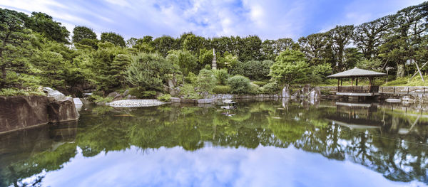 Central pond of mejiro garden which is surrounded by large flat stones under the foliage.