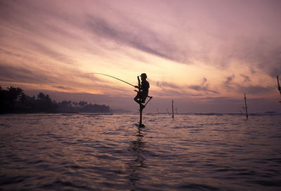 Silhouette of man fishing in sea against sky during sunset