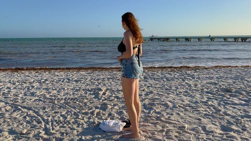 Young woman standing at beach against sky