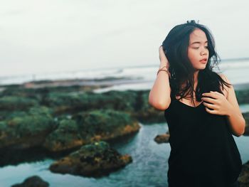 Young woman standing on rock by sea against sky