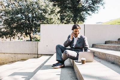 Young man looking away while sitting on retaining wall