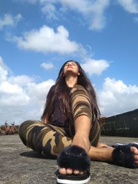 Woman sitting with arms raised against sky