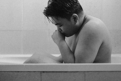 Side view of shirtless man sitting in bathroom