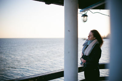 Young woman with eyes closed standing on pier over sea against clear sky
