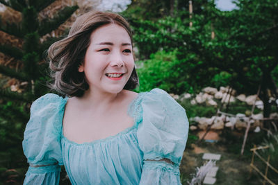 Smiling young woman looking away against trees