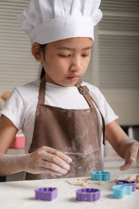 The little girl wore a white chef hat and a brown apron. the kid making cookies in the kitchen.