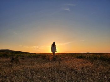 Rear view of woman standing on land against sky during sunset
