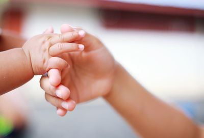 Cropped image of baby touching child hand at home