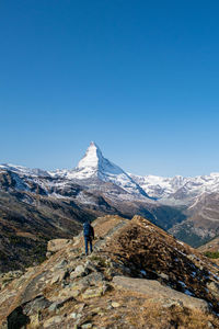 Rear view of man on snowcapped mountain against clear blue sky