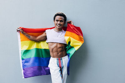 Man with rainbow flag standing against wall