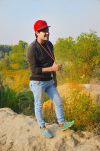 Young man looking away while standing on land against trees